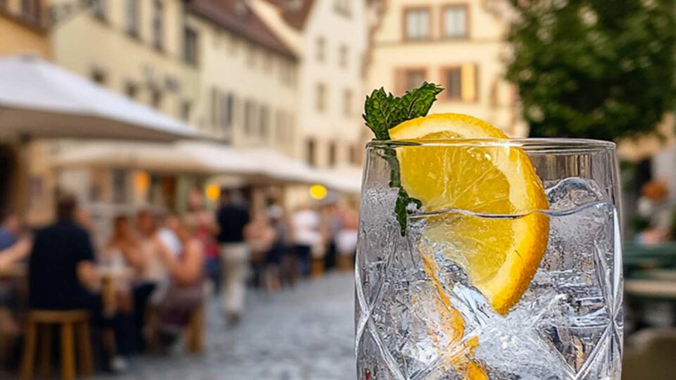 Das Bild zeigt ein gefülltes Gin-Glas vor einer Bayrischen Innenstadt